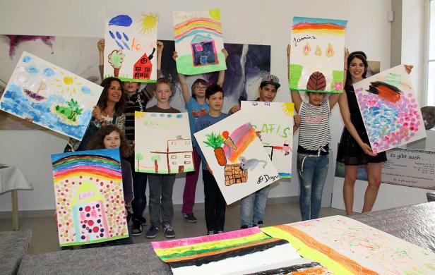 Eine Gruppe von Kindern und Erwachsenen präsentiert stolz ihre bunten Gemälde.