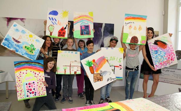 Eine Gruppe von Kindern und Erwachsenen präsentiert stolz ihre bunten Gemälde.