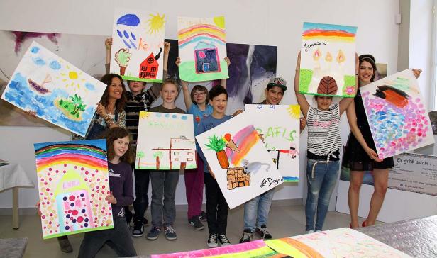 Eine Gruppe von Kindern und eine Frau präsentieren stolz ihre selbstgemalten Bilder.