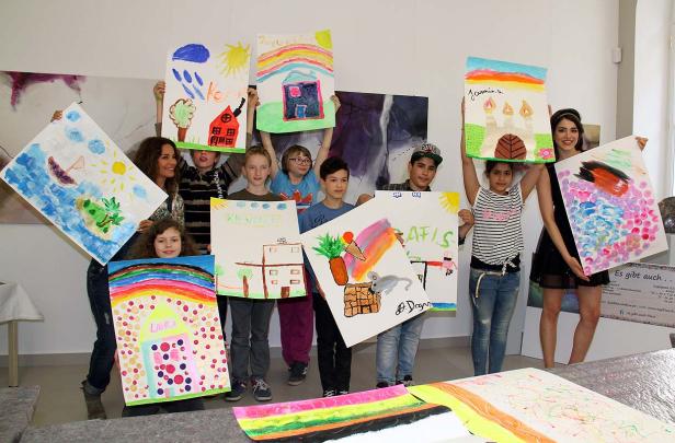 Eine Gruppe von Kindern und Erwachsenen präsentiert stolz ihre selbstgemalten Bilder.