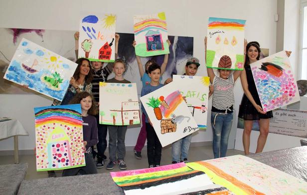 Eine Gruppe Kinder und eine Frau präsentieren ihre selbstgemalten Bilder.