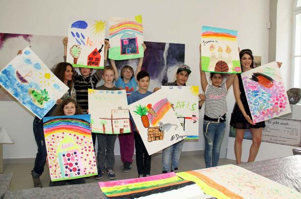 Eine Gruppe von Kindern und eine Frau präsentieren ihre bunten Gemälde mit Namen wie Laura, Kevin, Jaqueline, Jasmin und Rafis.