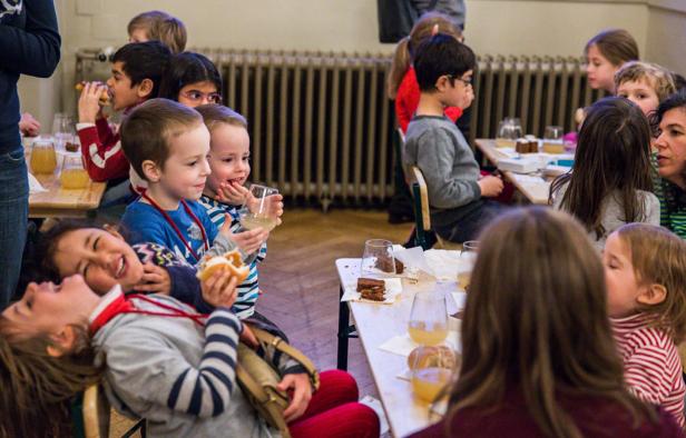 Eine Gruppe Kinder sitzt an Tischen und isst und trinkt.