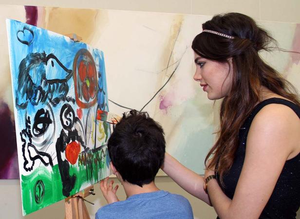 Eine Frau hilft einem Kind beim Malen eines abstrakten Bildes auf einer Leinwand.