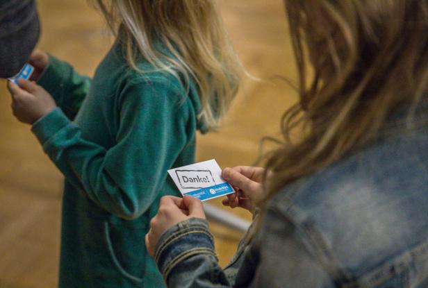 Zwei Kinder betrachten eine Karte mit der Aufschrift „Danke!“.