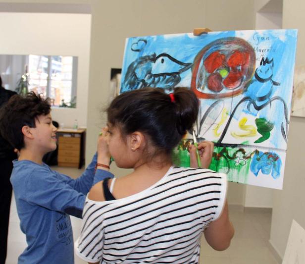 Ein Junge und ein Mädchen betrachten und bemalen ein großes, farbenfrohes Bild auf einer Staffelei.