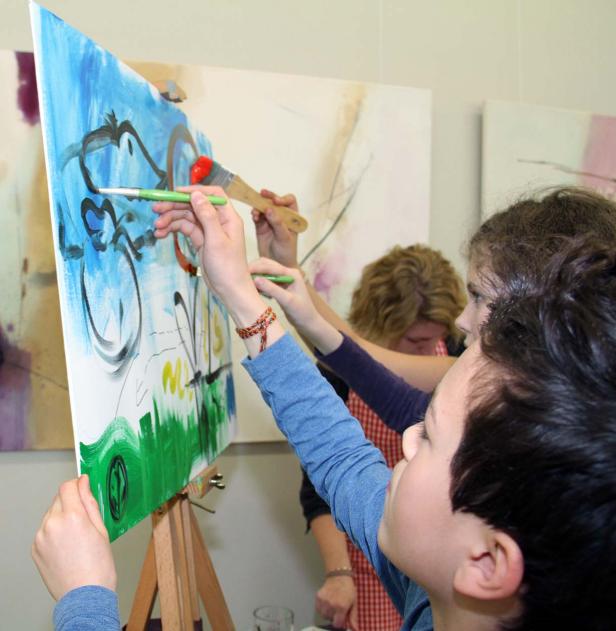 Kinder malen gemeinsam ein Bild auf einer Staffelei.