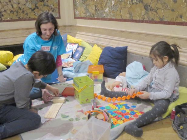 Eine Frau namens Irene spielt mit zwei Kindern mit Spielzeug auf dem Boden.