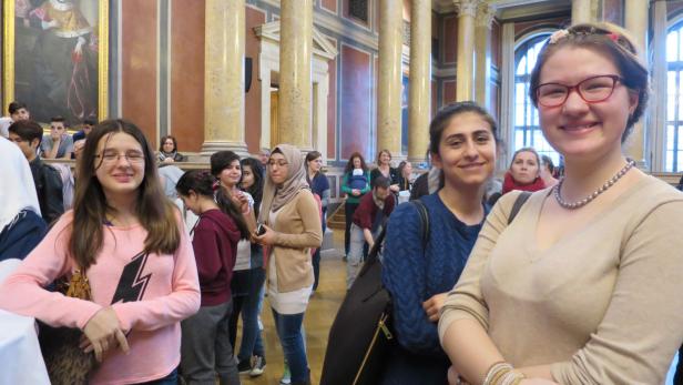 Eine Gruppe von Menschen steht in einem großen Saal mit Säulen und einem Gemälde.