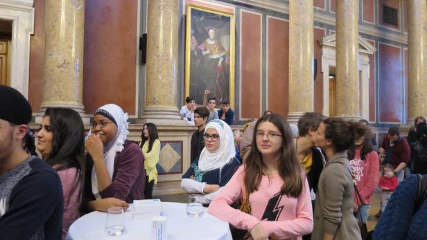 Eine Gruppe von Menschen steht in einem Raum mit Säulen und einem Gemälde.