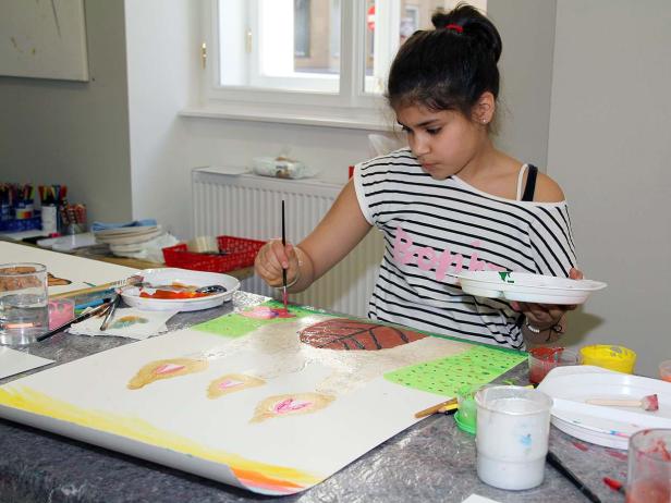 Ein junges Mädchen malt ein Bild mit einem Pinsel auf einer großen Leinwand.