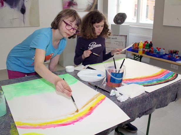 Zwei Mädchen malen Regenbögen mit Wasserfarben auf Papier.