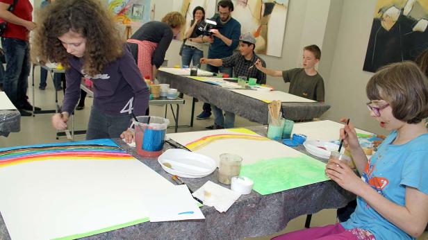 Kinder malen in einem Kunstatelier an Tischen mit Farben und Pinseln.