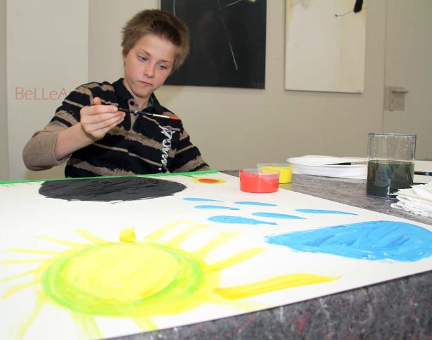 Ein Junge malt ein Bild mit Sonne, Wolken und einem schwarzen Loch.