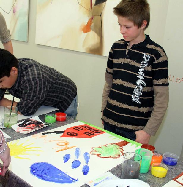 Zwei Jungen malen mit Wasserfarben auf einem großen Blatt Papier.