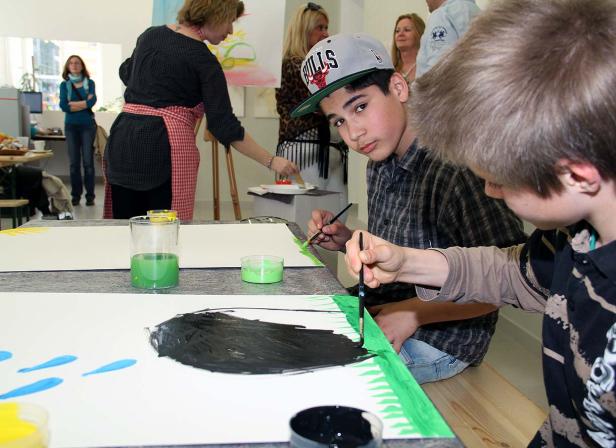 Jungen malen mit Pinsel und Farbe auf Papier in einem Kunstatelier.