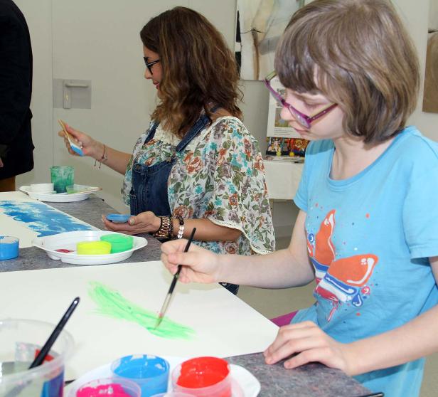 Zwei Frauen malen mit Pinseln auf Papier an einem Tisch.