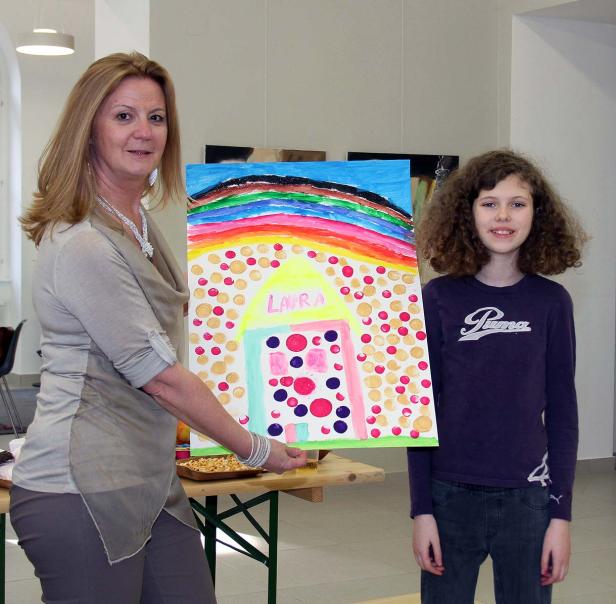 Eine Frau und ein junges Mädchen präsentieren ein farbenfrohes Kinderbild mit dem Namen „Laura“.