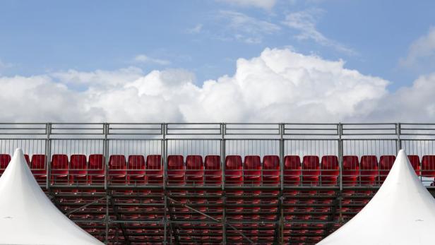 Leere rote Sitze auf einer Tribüne unter blauem Himmel mit Wolken.