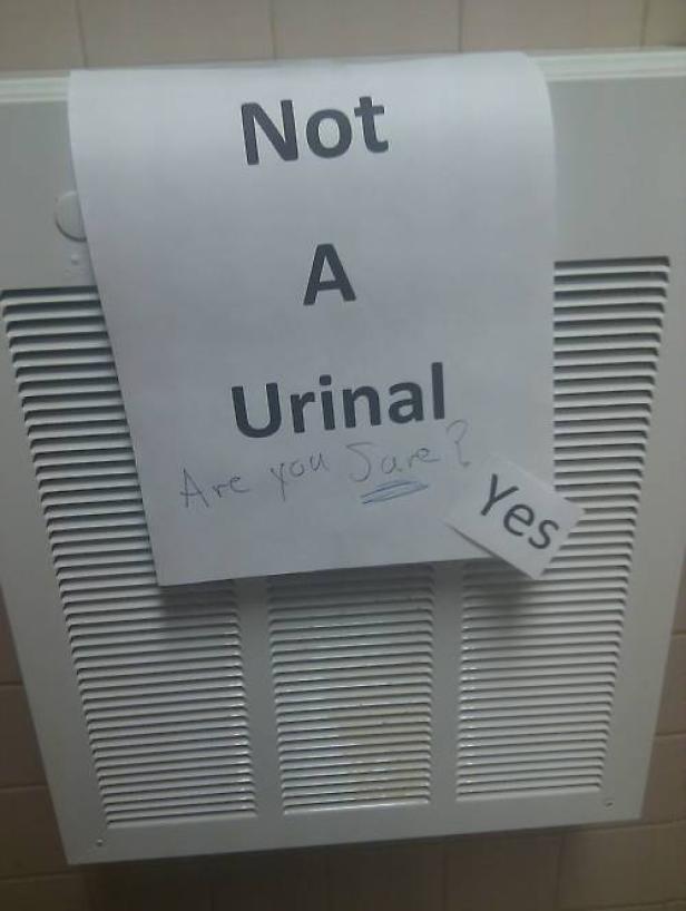 Ein Schild mit der Aufschrift „Not A Urinal. Are you sure? Yes“ hängt an einer weißen Gitterstruktur.