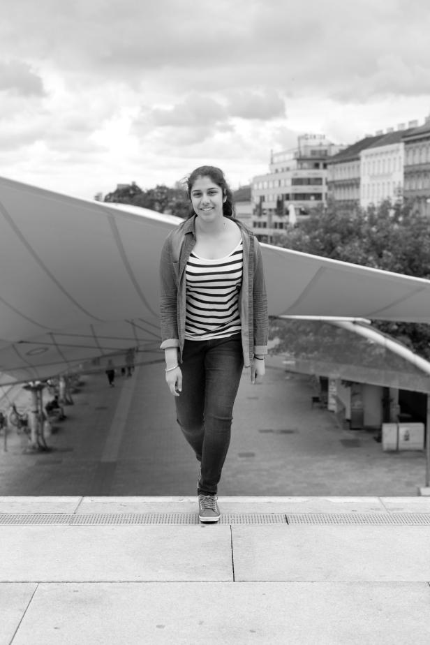 Eine junge Frau in Jeans und gestreiftem Oberteil steht vor einem Gebäude in Schwarzweiß.