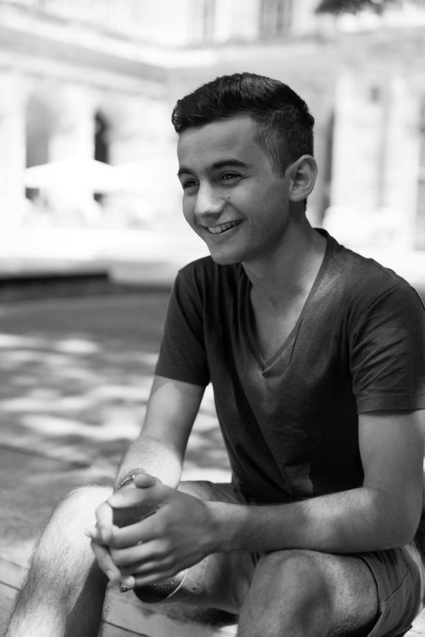 Ein junger Mann sitzt lächelnd im Freien.