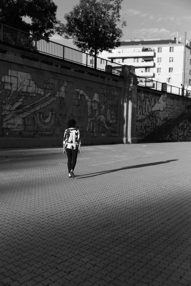 Eine Frau geht auf einem Platz mit Graffiti im Hintergrund entlang.