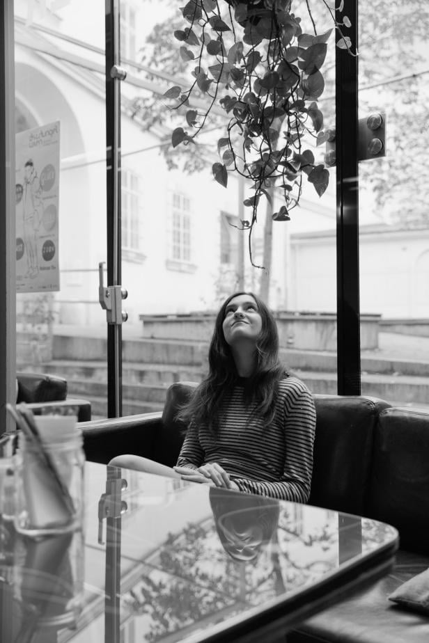 Eine junge Frau sitzt in einem Café und schaut nach oben.