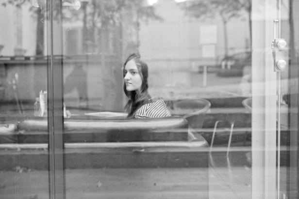 Eine junge Frau sitzt in einem Café, gesehen durch die Fensterscheibe.