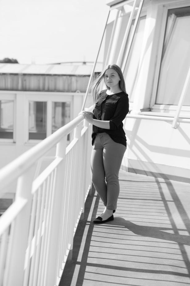 Eine junge Frau lehnt an einem Geländer auf einem Balkon.