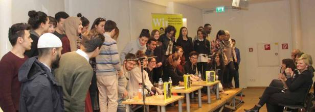 Eine Gruppe junger Menschen steht und sitzt auf einer Bühne bei einer Veranstaltung.