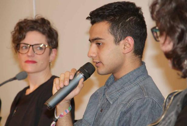 Ein junger Mann spricht bei einer Podiumsdiskussion in ein Mikrofon.