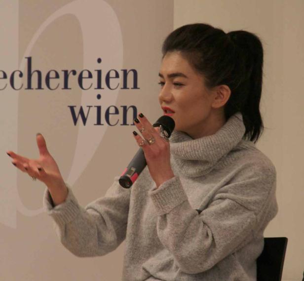 Eine Frau mit einem grauen Rollkragenpullover spricht in ein Mikrofon.