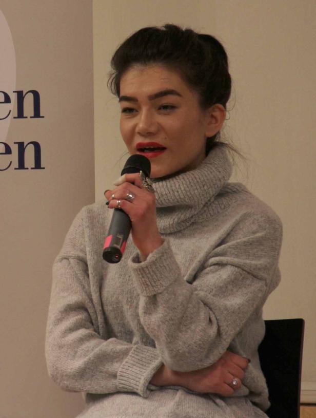 Eine Frau mit rotem Lippenstift spricht in ein Mikrofon.