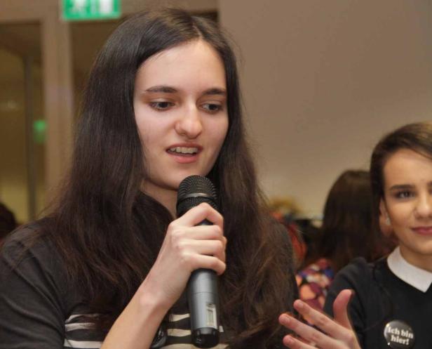 Eine junge Frau spricht in ein Mikrofon vor einem Publikum.