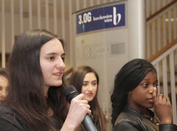 Eine junge Frau spricht in ein Mikrofon vor zwei weiteren Frauen.