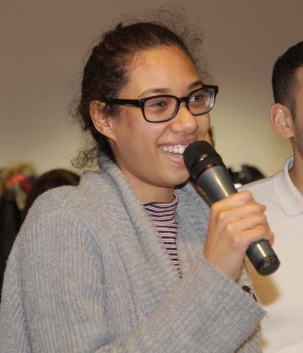 Eine junge Frau mit Brille spricht in ein Mikrofon.