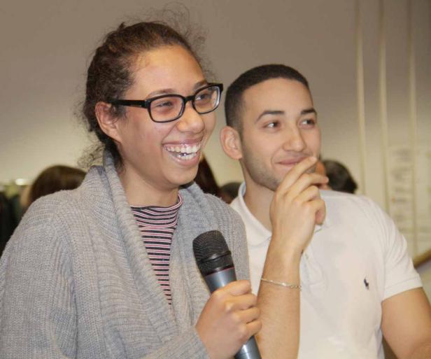 Eine lachende Frau mit Brille hält ein Mikrofon, neben ihr ein lächelnder Mann.