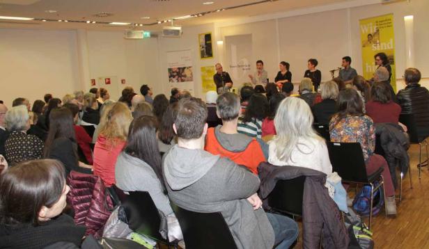 Publikum sitzt bei einer Podiumsdiskussion in einem Raum.
