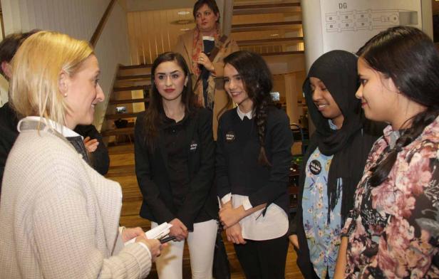 Eine Frau spricht mit einer Gruppe junger Frauen, die Buttons mit der Aufschrift „Ich bin hier!“ tragen.