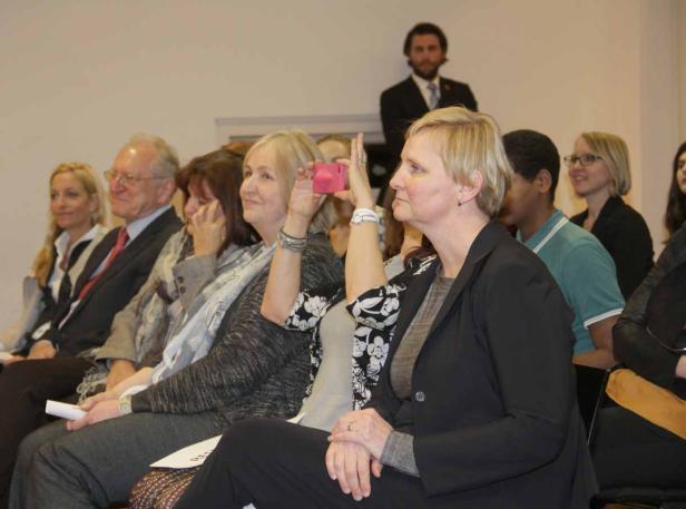Zuschauer sitzen bei einer Veranstaltung, eine Frau macht ein Foto mit ihrem Handy.
