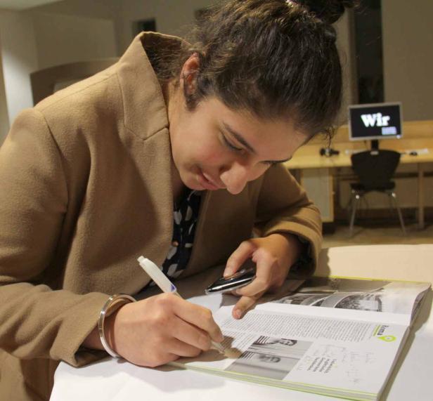 Eine Frau mit braunem Mantel liest und markiert einen Artikel in einer Zeitschrift.