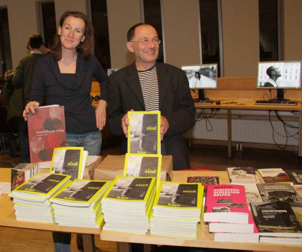 Eine Frau und ein Mann präsentieren Bücher des Mandelbaum Verlags auf einem Tisch.