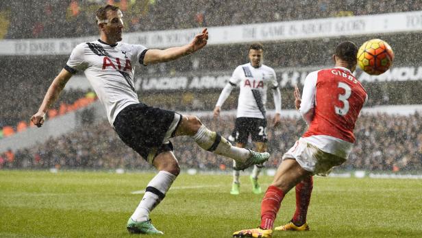 Ein Fußballspieler von Tottenham Hotspur schießt bei Regen einen Ball, während ein Gegenspieler von Arsenal zuschaut.