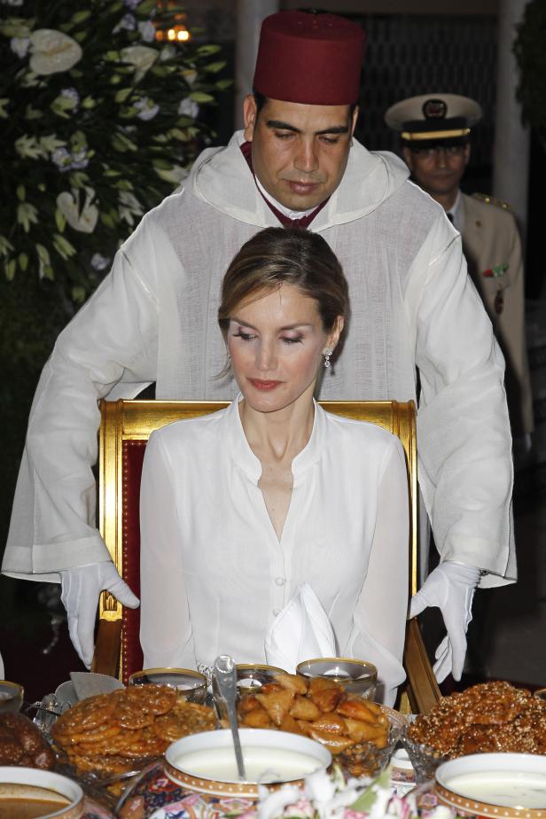 Königin Letizia sitzt an einem Tisch mit marokkanischen Süßigkeiten, während ein Mann in traditioneller Kleidung hinter ihr steht.
