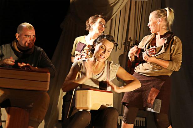 Eine Gruppe von vier Personen spielt auf der Bühne Musik mit verschiedenen Instrumenten.