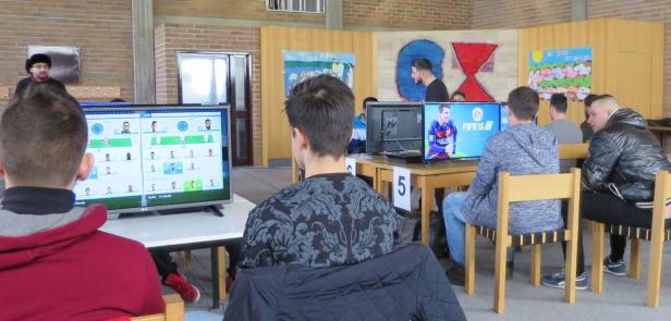 Mehrere Jugendliche spielen das Videospiel FIFA an Tischen in einem Raum.