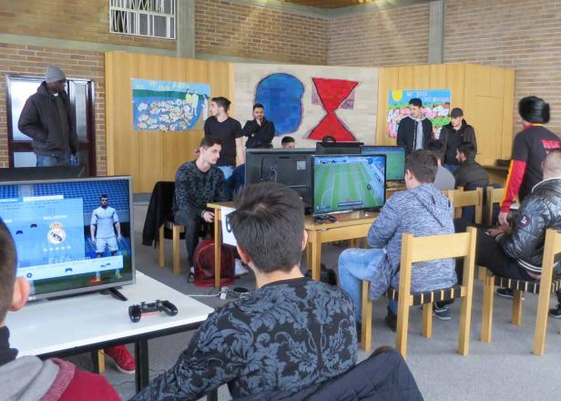 Mehrere Jugendliche spielen ein Fußball-Videospiel auf Bildschirmen in einem Raum.