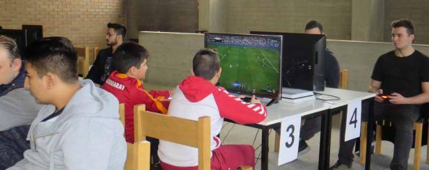 Mehrere Personen sitzen an Tischen und spielen ein Fußball-Videospiel.