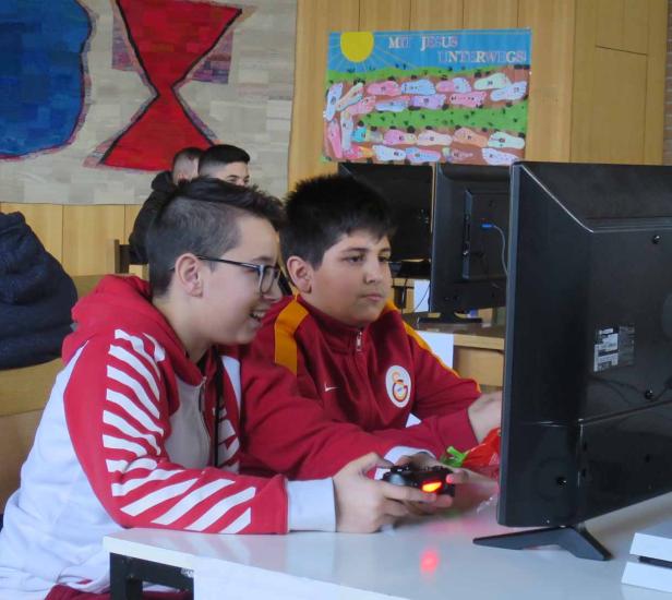 Zwei Jungen spielen ein Videospiel mit einem Controller vor einem Monitor.